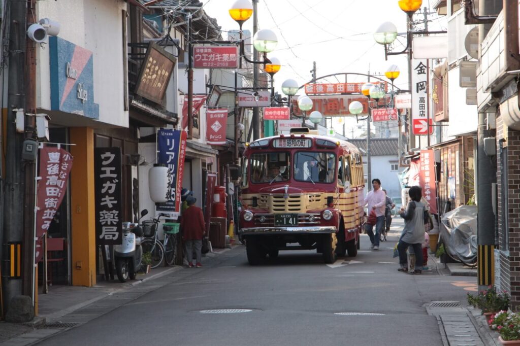 昭和の街で昭和時代のボンネットバスが商店街の通りを走る様子
