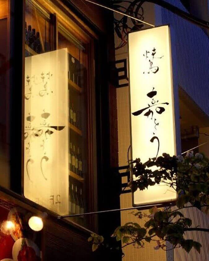 東京都にある地鶏の店「焼鳥 嘉とう」店前で明かりのついた看板を下から撮影
