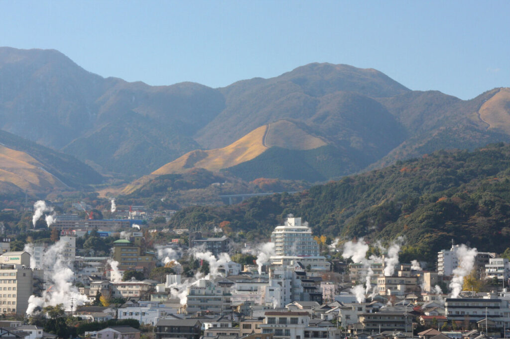 扇山を背景に湯煙が立ち上る別府温泉の街並み風景