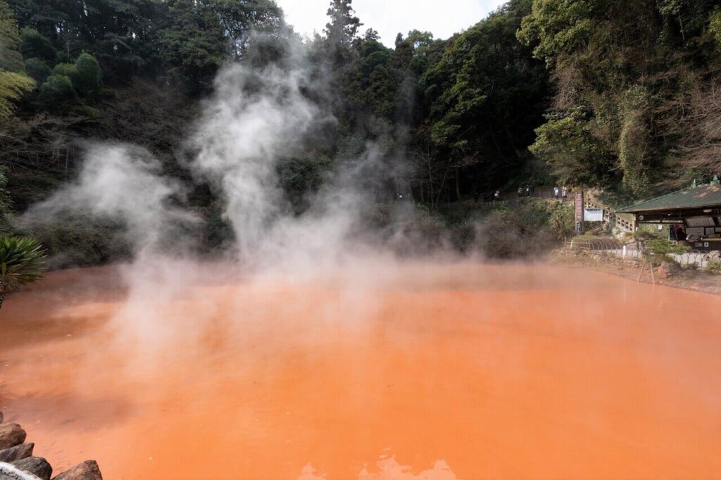 深紅に染まる血の池地獄。赤い湯面から湯気が立ちのぼる様子