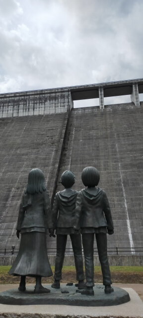 日田市大山ダムの進撃の巨人少年期像後ろ姿・エレンミカサアルミン像と巨大ダムの風景