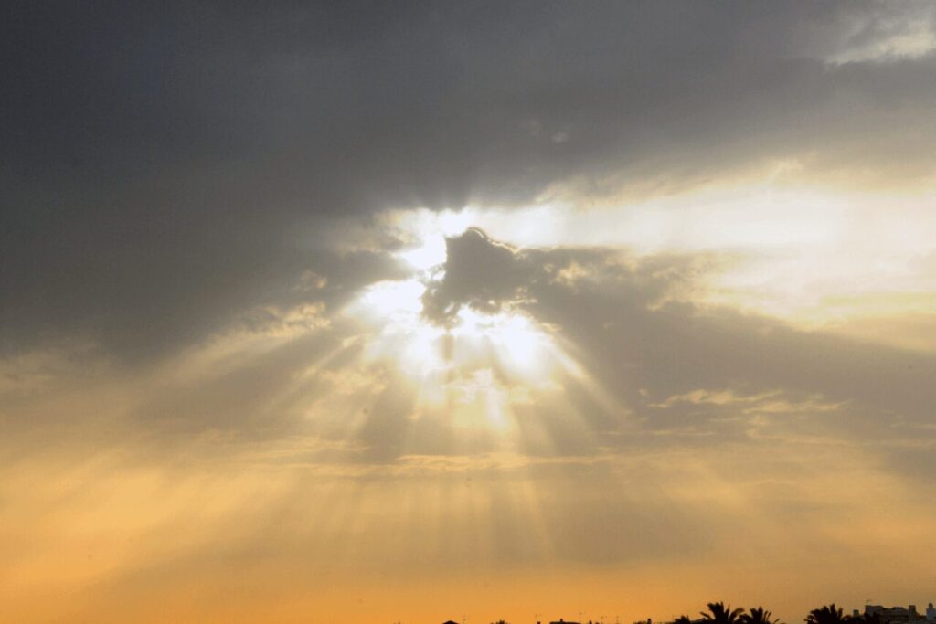 雲の切れ間から光が差す夕方の空、神聖な気配を感じる後光のイメージ