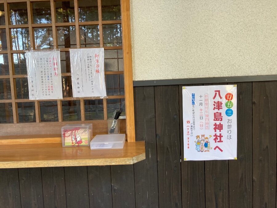 八津島神社の社務所受付窓口と、境内の案内やお知らせが掲示された張り紙(大分県日出町豊岡)
