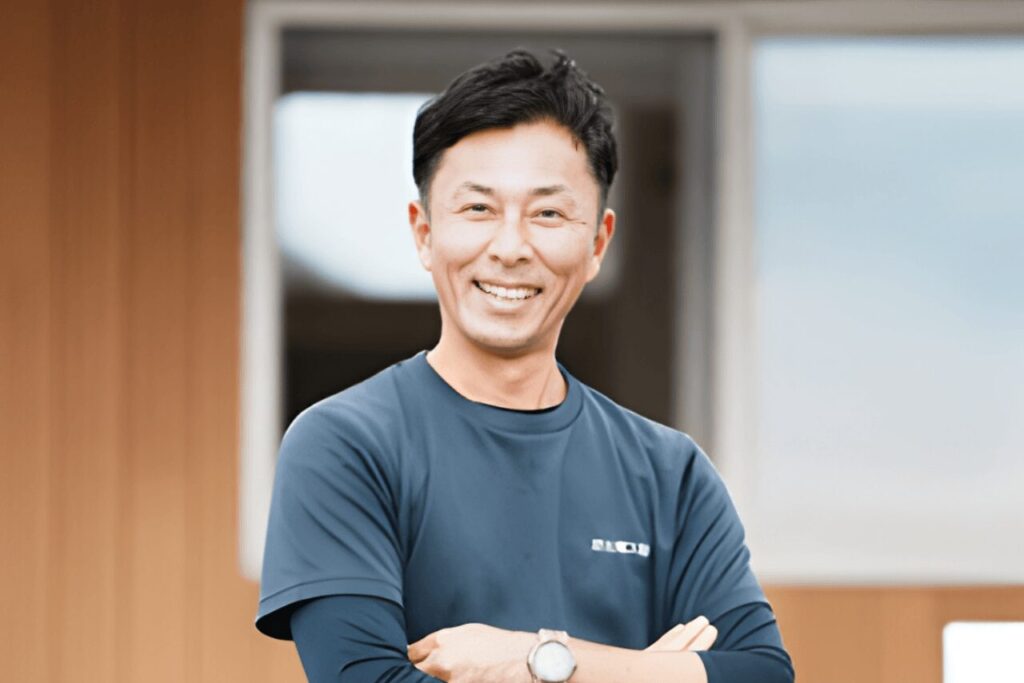 苅北電工代表の苅北さんが笑顔で腕組みをしている様子