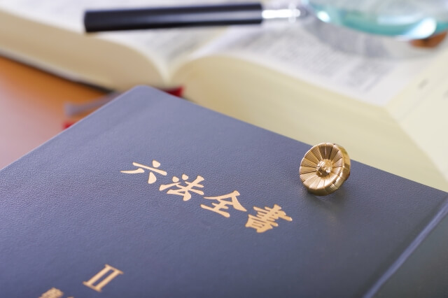 六法全書と弁護士バッジ、虫眼鏡が置かれた机 法律実務のイメージ
