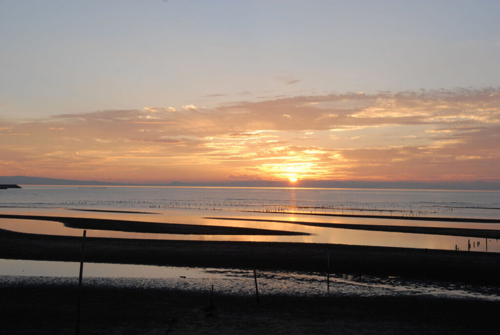 真玉海岸の干潟に映る夕陽と雲の隙間から沈む幻想的な夕日