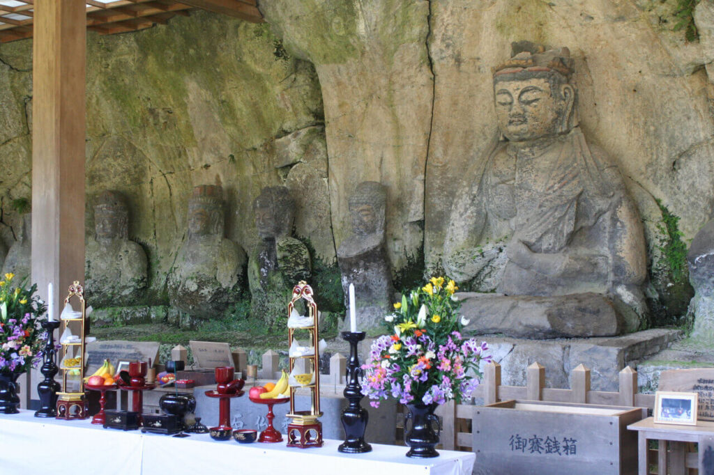 臼杵石仏 古園石仏前の供物と賽銭箱 左に並ぶ石仏群の全景(大分県臼杵市)