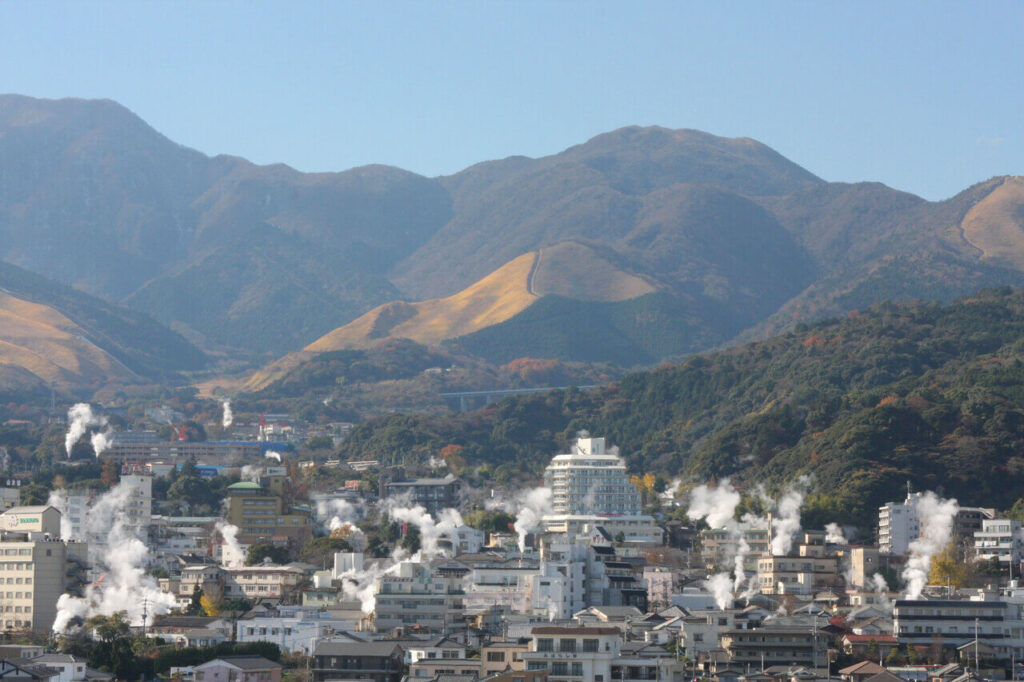 別府の山々を背景に、温泉街から湯気が立ち上る別府湯けむりの景色