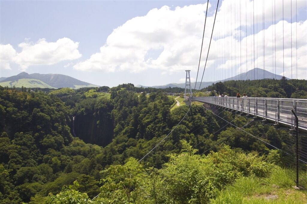 歩きやすい靴での観光がおすすめな、緑の渓谷と遠くのくじゅう連山を一望する大吊橋の入り口