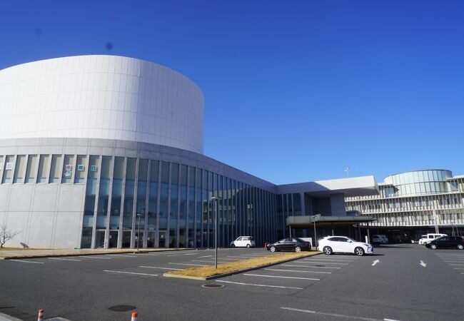 アストくにさきの外観。白い円筒形のホール棟とガラス張りの建物、青空