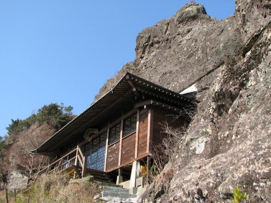 断崖の岩肌にせり出して建つ五辻不動尊のお堂と澄んだ青空