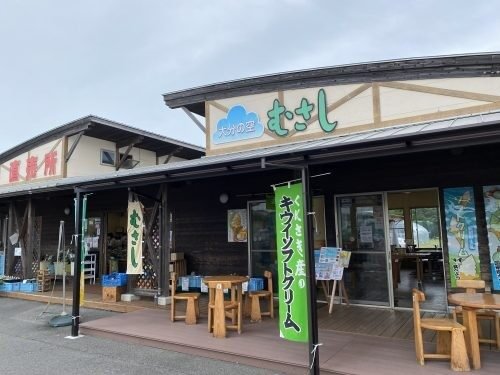 大分の空 むさしの店頭。「むさし」の看板とくにさき産キウイソフトクリームの幟、木のベンチが並ぶ直売所