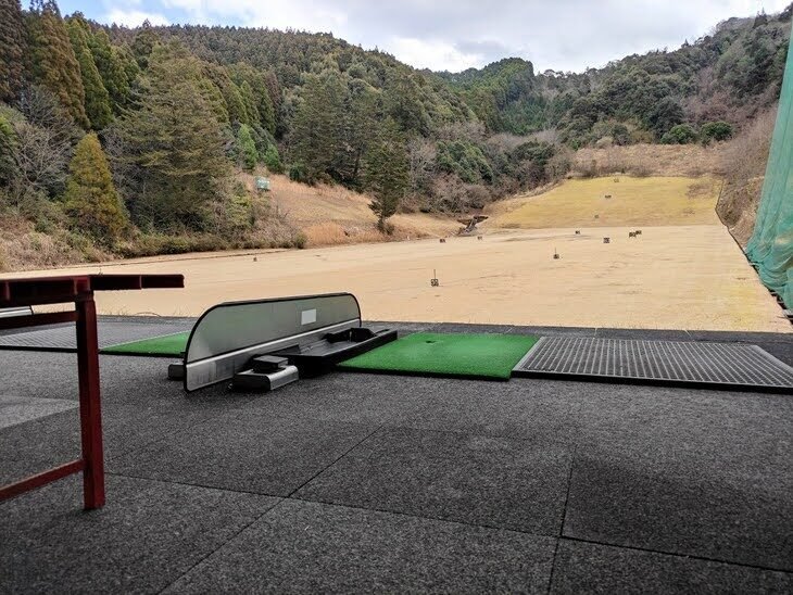 打席から見たグリーンパーク直川ゴルフ練習場のフィールド全景。山に囲まれた広大な芝のエリアに距離標識が並ぶ